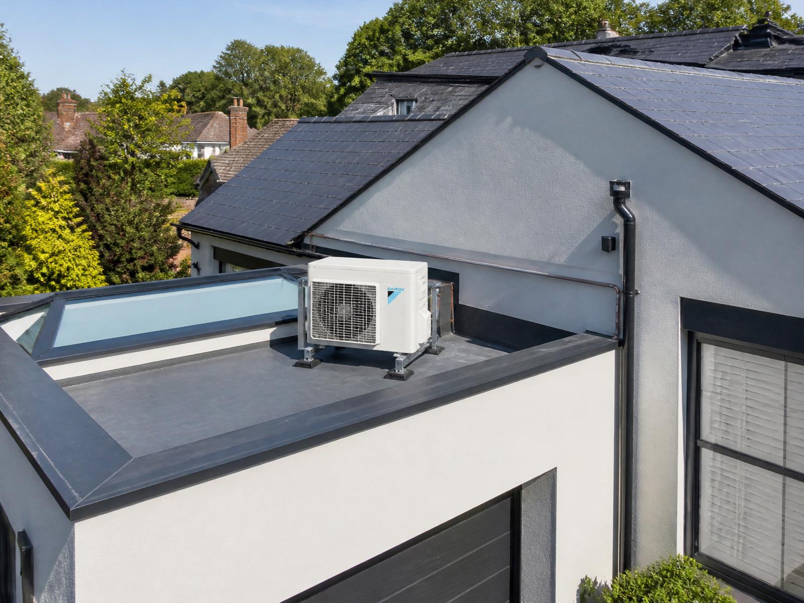White Daikin outdoor condenser discreetly installed on a flat roof section behind a parapet